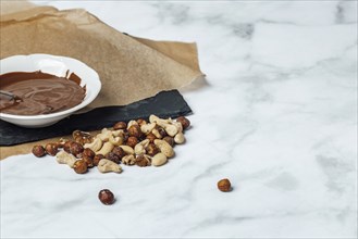 Chocolate icing in white bowl on baking paper, nut mixture, copy space