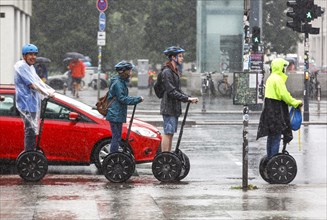 Tourists standing at a traffic light in heavy rain with Segway personal transporters, Berlin, 23 06