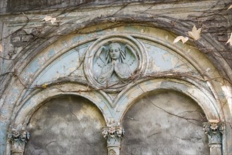 Relief of an angel on a dilapidated blue façade, historical angel, praying, tomb with round arches