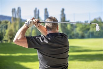 Golfer Making a Golf Swing with His 6 Iron Golf Club in a Sunny Day in Switzerland