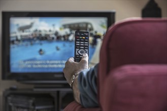 Man in comfy chair switching channels with remote control to look for pleasing programme on