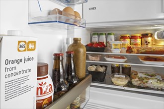 Cooled food and beverages in open fridge, refrigerator in kitchen