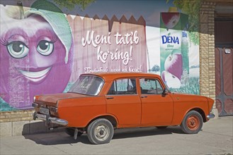 Old Trabant parked in front of advertisement painted on wall in Uzbekistan