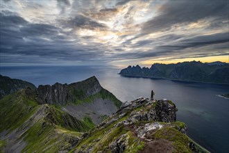 Hiker standing on summit, fjord and mountains, mountain range Okshornan in the back, Senja, Norway,