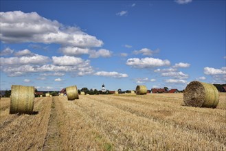 Straw bales on a harvested grain field, in the background the village church with onion tower,