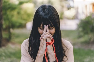 Woman practicing meditation sitting in yoga asana Kali Mudra holding a japa mala outdoors