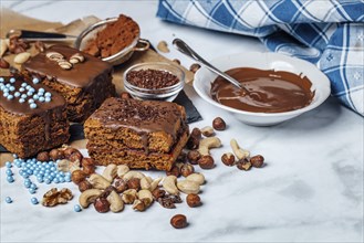 Brownies filled with jam surrounded by ingredients for decoration, chocolate icing, mixed nuts,