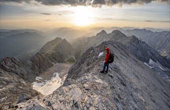 Mountaineer with helmet on a narrow mountain ridge at sunrise, crossing the JubilÃ¤umsgrat, view of