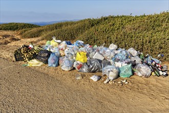 Mountain of rubbish, rubbish bags, plastic waste and old glass in front of a dune landscape by the