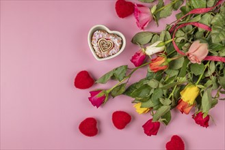 Colourful bouquet of roses with red hearts and heart-shaped bowl with muffin on a pink background