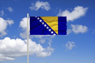 National flag of Bosnia and Herzegovina, in front of cumulus clouds and blue sky, studio