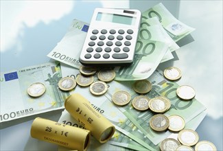 A pocket calculator and euro banknotes next to coins, studio shot