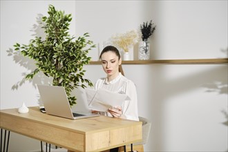 Woman checking tax return sitting in bright office at a desk with laptop