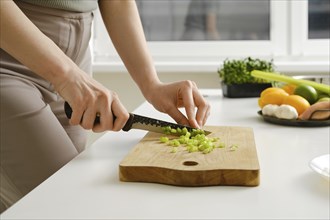 Hands of young woman chopping fresh celery on wooden board while preparing food