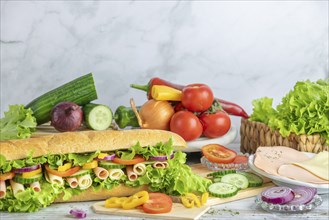 A large filled sandwich next to freshly cut vegetables, sausage and salad, copy room