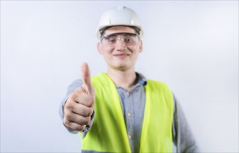 Smiling young engineer gesturing approval with thumb. Cheerful engineer giving thumbs up to the