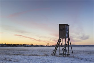 Raised hide for hunting roe deer at sunrise in snow covered field in winter, Lower Saxony, Germany,