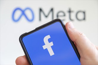 Hand holding mobile phone with Facebook and Meta logo social media computer screen