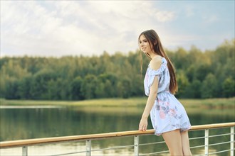 Happy young woman looking at the river leaning on railing on the pier