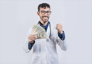 Smiling young doctor holding money isolated. Cheerful doctor holding dollars bills isolated