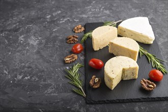 Cheddar cheese and various types of cheese with rosemary and tomatoes on black slate board on a