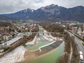 Cityscape with river running under a bridge, surrounded by buildings, streets and mountains in the