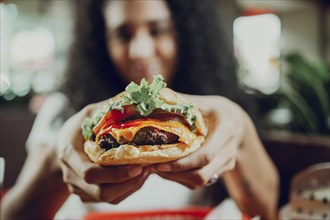 Close-up of a girl showing appetizing hamburger in a restaurant. Hands of girl showing burger in a