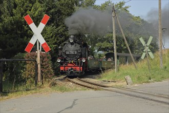 Fichtelbergbahn steam train over ungated level crossing with St. Andrew's cross at station, tourist