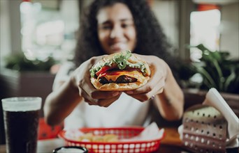 Smiling girl showing a burger in a restaurant. Close-up of a woman showing appetizing hamburger in