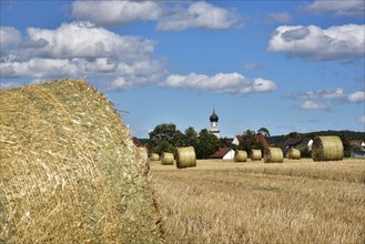 Straw bales on a harvested grain field, in the background the village church with onion tower,