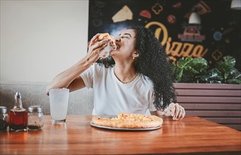 Lifestyle of afro-haired woman enjoying a pizza in a restaurant. Happy afro hair woman eating pizza