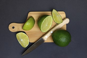 Halved limes on a chopping board with a kitchen knife