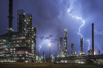 Lightning bolts striking over oil refinery at industrial estate during heavy thunderstorm at night,