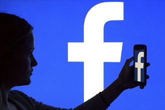 Silhouette of a woman with a smartphone in her hand in front of a Facebook logo, 12/01/2016