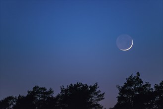 Very narrow, fine crescent moon with visible moon disc stands one day after the new moon over a