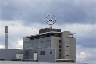 Mercedes star in front of dark clouds, office building at the headquarters of Mercedes-Benz Group