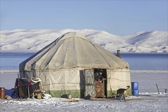 Kyrgyz man in door opening of traditional yurt in the snow along Song Kul, Song Kol lake in the