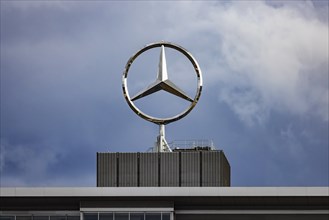 Mercedes star in front of dark clouds, office building at the headquarters of Mercedes-Benz Group