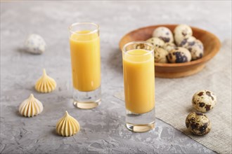 Sweet egg liqueur in glass with quail eggs and meringues on a gray concrete background. Side view,