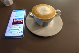 Cappuccino, next to it a mobile phone on the table Bavaria, Germany, Europe