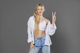 Happy woman showing victory sign on grey studio background