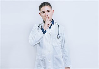 Doctor making silence gesture on white background. Latin doctor silencing and looking at the camera