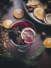 Glass of traditional mulled wine with orange and cranberry garnishes on a cozy Christmas table. The