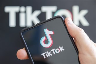 Hand holding mobile phone with TikTok logo social media with computer screen