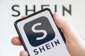 Hand holding mobile phone with Shein logo online marketplace online trading ecommerce computer