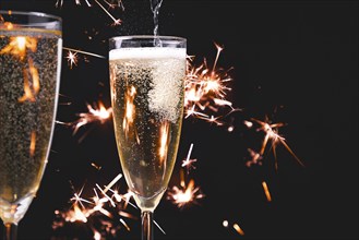 Two champagne glasses, pouring champagne, fireworks, dark background, copy room