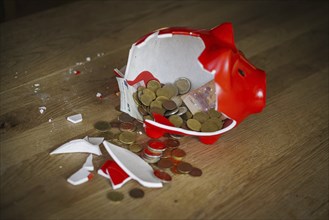 Symbolic photo on the subject of saving. An open, broken piggy bank with coins and banknotes stands