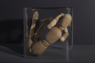 Wooden mannequin locked in a glass cube on gray background. captivity, break rules, loneliness,