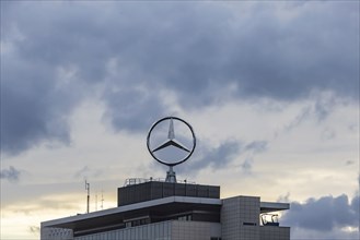 Mercedes star in front of dark clouds, office building at the headquarters of Mercedes-Benz Group