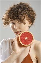 Woman holds half of grapefruit in hand next to her face